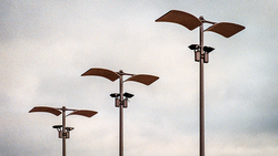 Three rusty metal wind vanes of increasing height arranged in a receding line against an overcast sky.