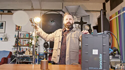 Photographer holding a reflector in a studio filled with lighting equipment and props.