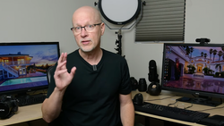 Man in black shirt gesturing while speaking in a studio with multiple monitors displaying architectural photography.