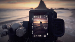 Camera display screen showing live view of a coastal rock formation at sunset during golden hour.
