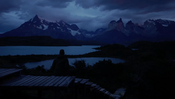 Silhouetted figure sitting on a wooden deck overlooking a mountain lake at dusk.