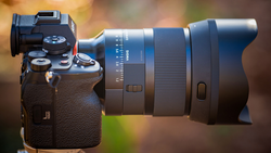 Mirrorless camera body with attached zoom lens mounted on a stand against a blurred bokeh background.