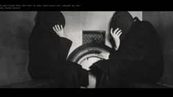 Two figures in dark clothing hide their faces with their hands while sitting near a large cylindrical metal object.