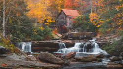 Historic gristmill with red roof beside cascading waterfall in autumn forest.
