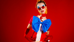 Person wearing red and white outfit with oversized blue bow against red background.