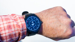 Smartwatch with blue digital display showing compass heading and temperature on wrist wearing red plaid shirt.