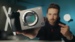 Photographer holding a mirrorless camera body with visible sensor and a ring light in studio setting.