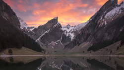 Alpine lake reflecting snow-capped mountains under a vibrant sunset sky.