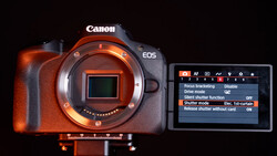 Canon EOS camera body with exposed sensor and rear LCD screen displaying menu settings.