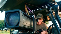 Cinematographer operating a large cinema camera mounted on a crane arm outdoors.