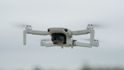 White compact drone photographed from below against an overcast sky.