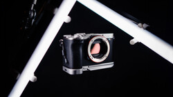 Mirrorless camera body with open shutter displayed against black background with white frame border.