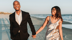 Couple holding hands while walking on a beach at sunset.