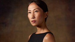 Woman in black sleeveless top against warm, blurred brown background, gazing to the side.