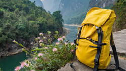 Bright yellow backpack resting on a rocky outcrop overlooking a misty mountain valley and river below.