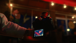 Hand holding a camera with live thermal imaging displayed on its rear screen during an evening event.