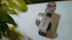 Silver rangefinder camera with dual rewind knobs viewed from above on white surface with green plant leaf in frame.