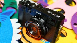 Rangefinder camera with orange lens ring on colorful abstract background.