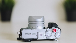 Silver Fujifilm X100VI rangefinder camera with lens cap and red shutter button visible on top.
