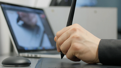 Person holding a stylus or pen tool while viewing an image on a laptop screen.
