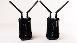 Two black wireless transmission units with dual antennas positioned side by side against a white background.