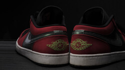 Rear view of red and black sneakers with white sole and gold wing logo embroidery.