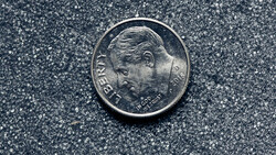 Close-up of a silver coin with a profile portrait facing left on a textured gray surface.