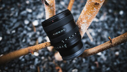 Black camera lens suspended among bare branches against a dark textured background.