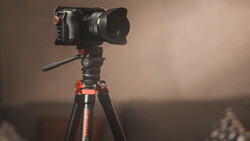 Professional cinema camera mounted on tripod with fluid head and extended lens hood.