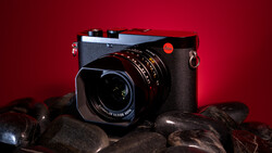 Leica rangefinder camera with mounted lens on dark rocks against deep red background.