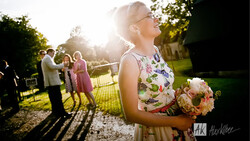 Bride in floral dress holding peach bouquet at outdoor garden wedding ceremony during golden hour.