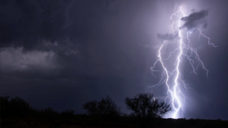 Jagged lightning bolt striking ground during nighttime thunderstorm with dark storm clouds.