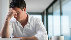Man in white shirt with hand to face, appearing stressed or contemplative at desk.