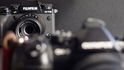 Fujifilm X-T5 mirrorless camera in sharp focus with additional camera gear blurred in the background.