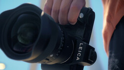 Photographer holding a mirrorless camera with a wide-angle lens against a blue sky background.