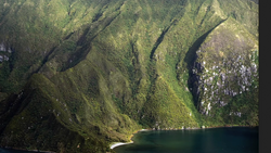 Steep forested valley with a narrow river and dramatic moss-covered cliff faces.