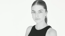 Portrait of a woman with pulled-back hair wearing a black sleeveless top against a white background.