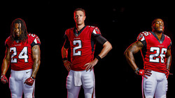 Three football players in red jerseys posed against black background.