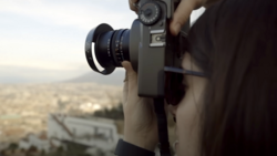 Photographer holding a vintage film camera with telephoto lens, capturing an aerial cityscape view.