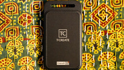 T-CREATE portable device with black casing displayed on colorful patterned fabric background.