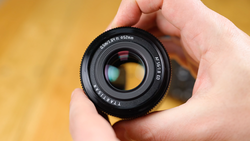 Hand holding a Canon 50mm f/1.8 lens with yellow background.