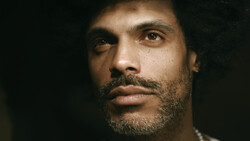 Man with beard looking directly at camera against dark background.