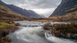 Mountain river flowing through a valley with dramatic peaks and overcast sky.