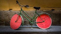 Green bicycle with watermelon-designed wheels leaned against a weathered yellow and gray wall.