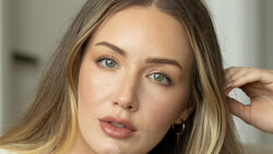 Woman with long brown hair and green eyes looking directly at camera with neutral expression.
