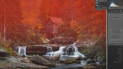 Waterfall flowing over rocks with autumn foliage and a red mill house in the background.