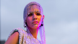 Portrait of a person with beaded braids and bold makeup against a twilight sky with warm and cool color grading.