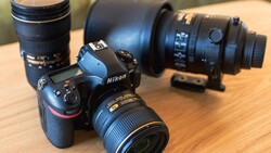 Nikon DSLR camera with attached lens surrounded by additional lenses on wooden surface.