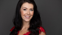 Woman with long black hair smiling at camera against gray background.