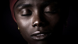 Close-up portrait of a person with eyes closed, dramatically lit against a dark background with warm side lighting.